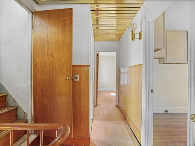 hallway featuring wooden walls, light wood finished floors, stairway, and a wainscoted wall
