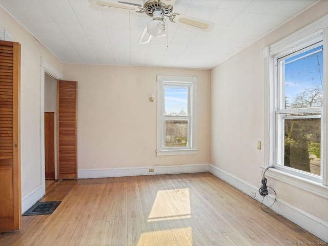 empty room with light wood-type flooring, a ceiling fan, baseboards, and a wealth of natural light