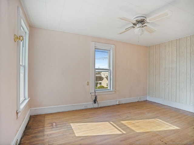 unfurnished room with wood-type flooring, a ceiling fan, baseboards, and wood walls