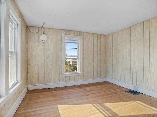 empty room with wooden walls, visible vents, and wood finished floors