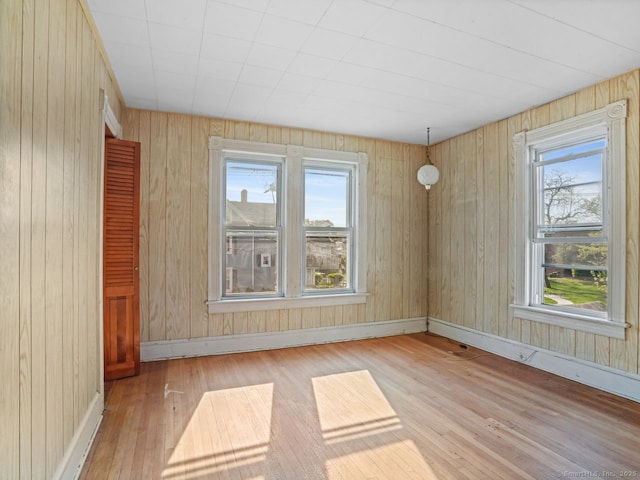 unfurnished room with baseboards, wood walls, a wealth of natural light, and hardwood / wood-style floors