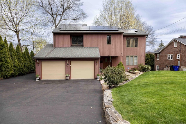 view of front of home with a garage, roof mounted solar panels, a front lawn, and driveway