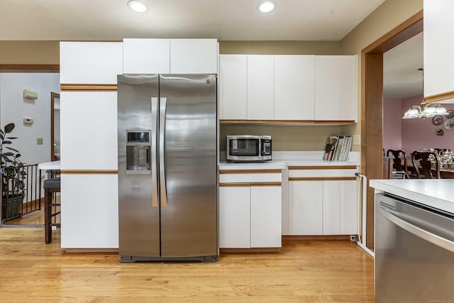 kitchen with appliances with stainless steel finishes, light wood finished floors, light countertops, and white cabinets