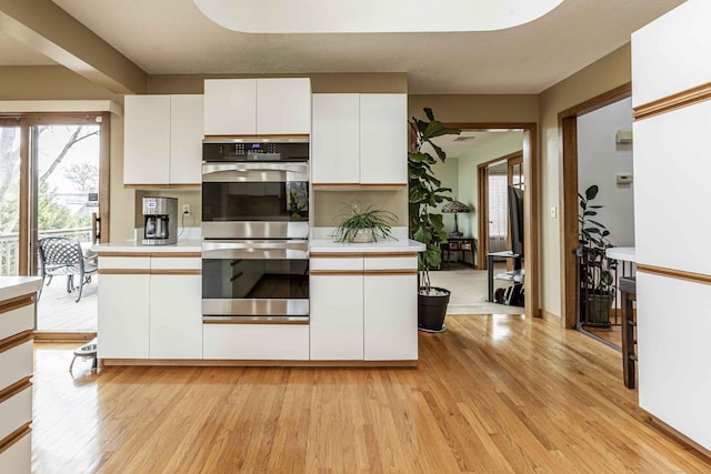 kitchen featuring light wood-type flooring, stainless steel double oven, white cabinetry, and light countertops