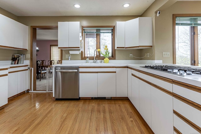 kitchen with light wood-style floors, white cabinetry, stainless steel dishwasher, and a sink