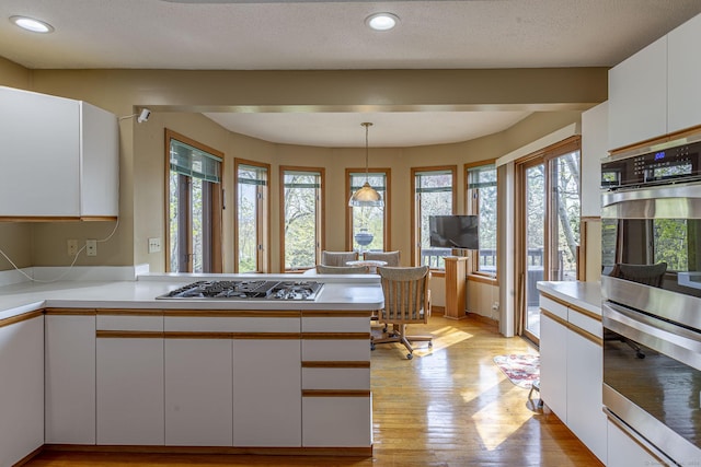 kitchen with white cabinetry, appliances with stainless steel finishes, light countertops, light wood-type flooring, and a peninsula