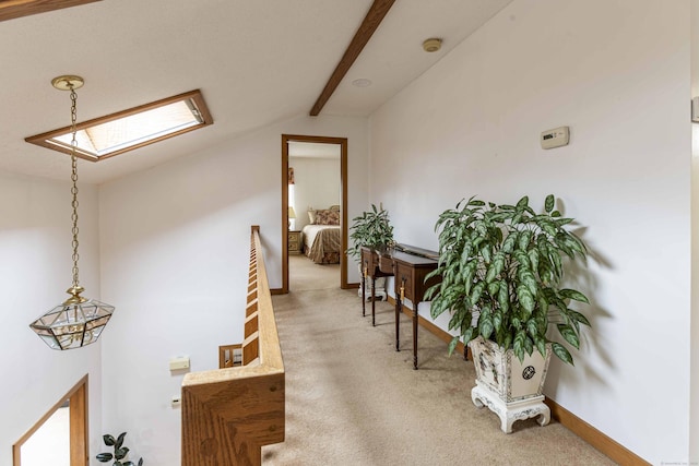 hall featuring light colored carpet, baseboards, and vaulted ceiling with skylight