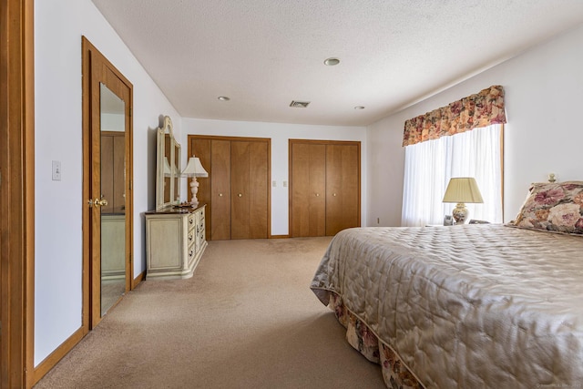 carpeted bedroom with a textured ceiling, two closets, baseboards, and visible vents