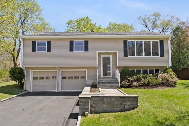raised ranch featuring an attached garage, a front yard, and aphalt driveway