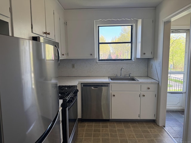 kitchen featuring range with gas stovetop, a sink, light countertops, stainless steel dishwasher, and freestanding refrigerator