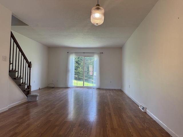 empty room featuring dark wood-style floors, visible vents, stairway, and baseboards