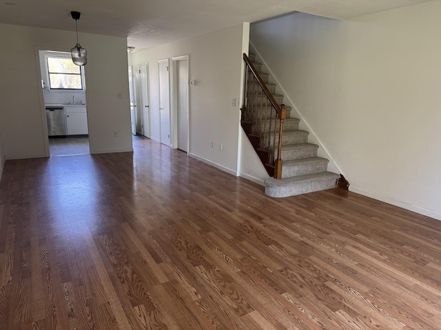 unfurnished living room featuring baseboards, stairway, dark wood-style flooring, and a sink