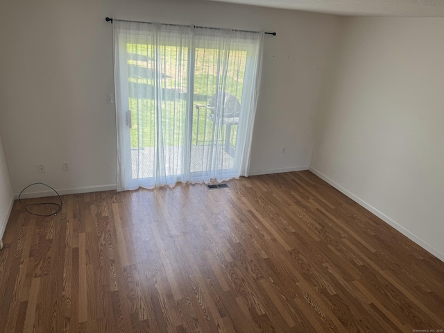 unfurnished room with dark wood-style floors, visible vents, and baseboards