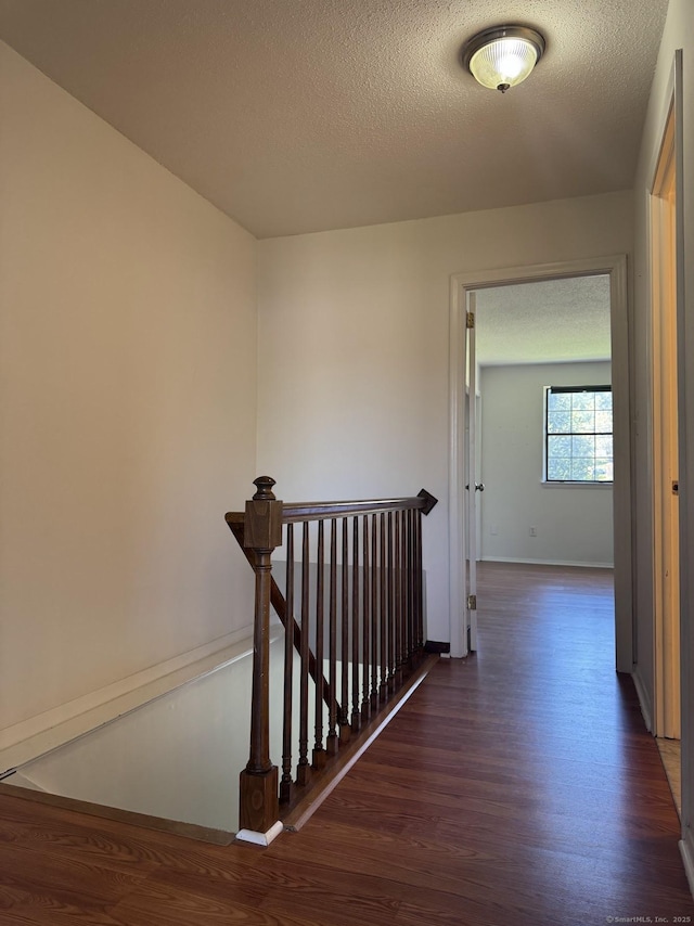 staircase with a textured ceiling, wood finished floors, and baseboards
