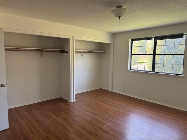 unfurnished bedroom with a textured ceiling, multiple closets, dark wood-style floors, and baseboards
