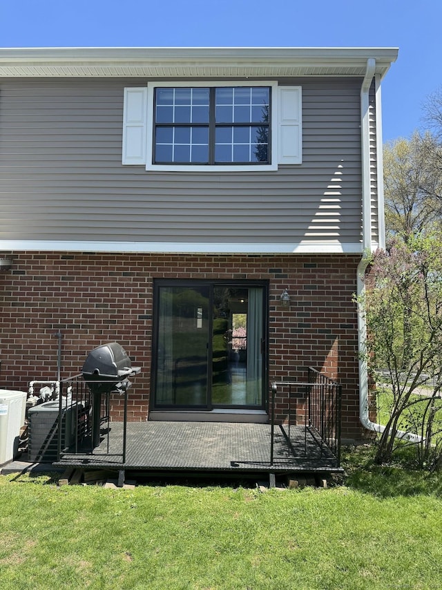 rear view of property with a deck, a yard, and brick siding