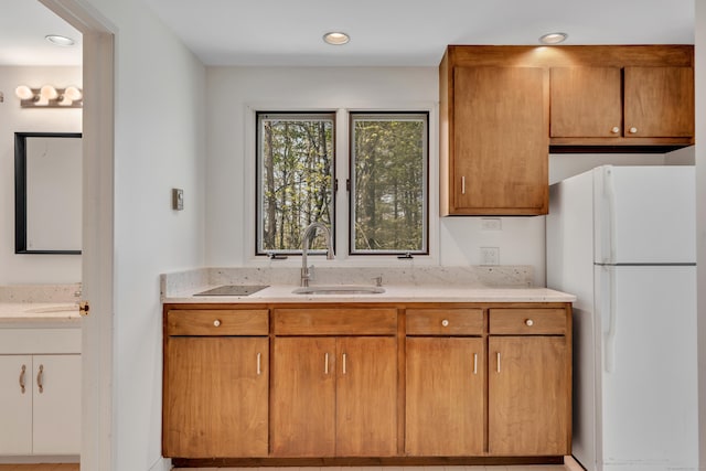 kitchen with light stone counters, freestanding refrigerator, a sink, and recessed lighting