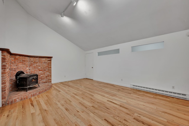 unfurnished living room featuring a wood stove, lofted ceiling, baseboards, a baseboard radiator, and light wood finished floors