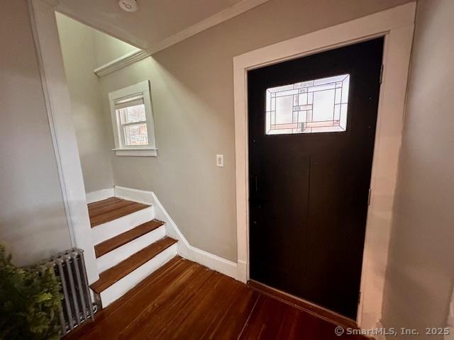 foyer entrance with crown molding, radiator, stairs, baseboards, and dark wood-style floors