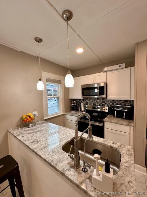 kitchen featuring pendant lighting, white cabinetry, tasteful backsplash, light stone counters, and stainless steel appliances