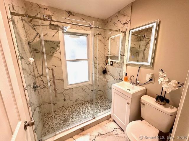 bathroom featuring toilet, a marble finish shower, marble finish floor, and vanity