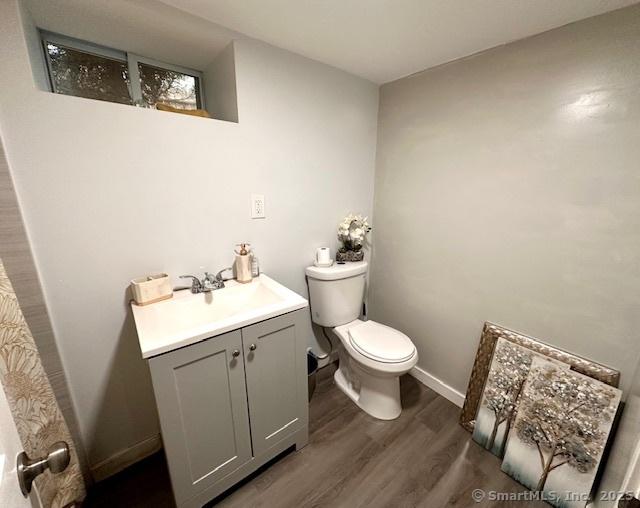 bathroom featuring toilet, baseboards, wood finished floors, and vanity