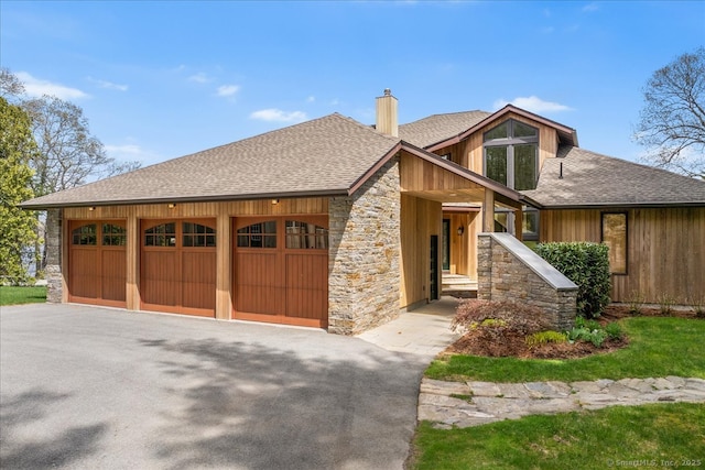 view of front of home with roof with shingles, an attached garage, aphalt driveway, stone siding, and a chimney