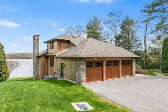 exterior space with a garage, stone siding, a chimney, a shingled roof, and a yard
