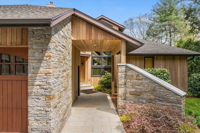 doorway to property featuring roof with shingles, a chimney, and stone siding