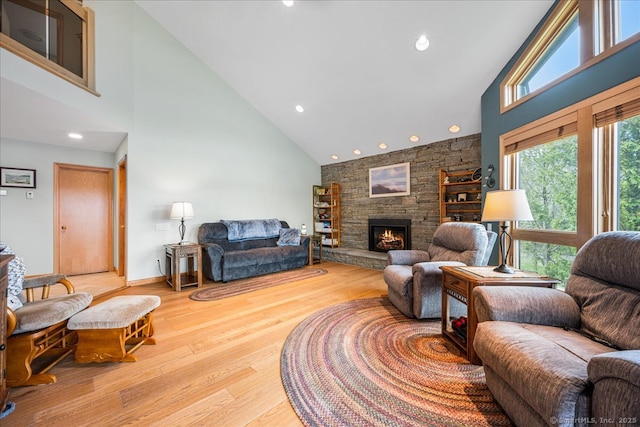 living room with recessed lighting, high vaulted ceiling, a stone fireplace, and wood finished floors