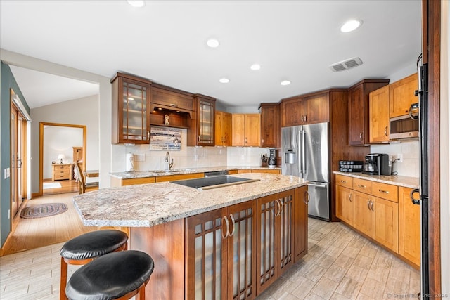 kitchen with a sink, stainless steel appliances, decorative backsplash, light wood-type flooring, and visible vents