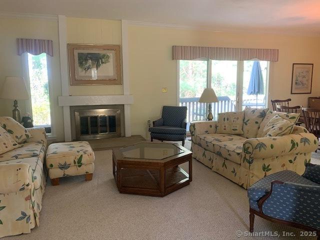living room with a glass covered fireplace, crown molding, and carpet flooring