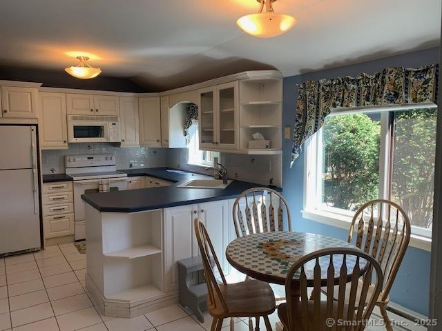 kitchen featuring dark countertops, open shelves, vaulted ceiling, and white appliances