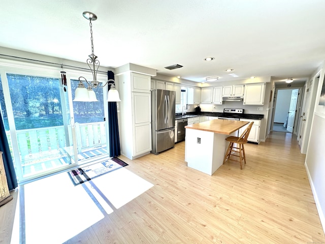 kitchen featuring appliances with stainless steel finishes, a sink, light wood-style floors, under cabinet range hood, and butcher block countertops