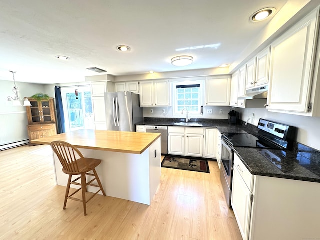 kitchen featuring appliances with stainless steel finishes, a sink, light wood-style flooring, under cabinet range hood, and a kitchen island