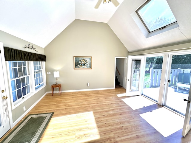interior space featuring ceiling fan, baseboards, lofted ceiling with skylight, and light wood-style floors