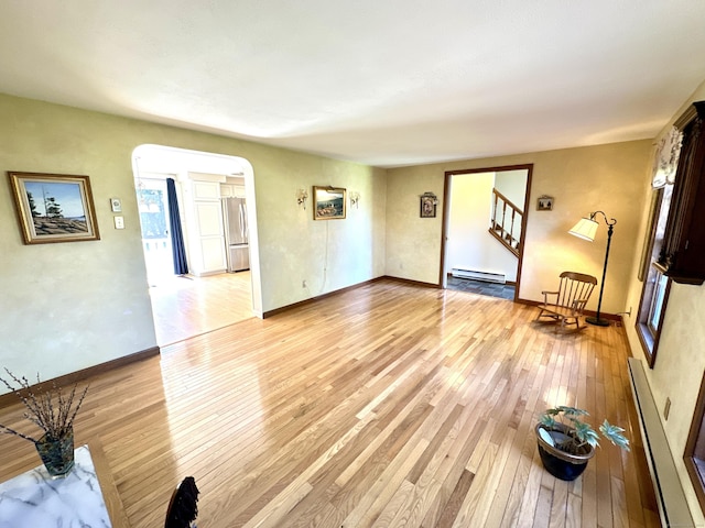 unfurnished living room featuring light wood-style floors, a baseboard radiator, arched walkways, and stairway