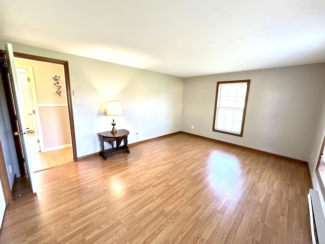 spare room with baseboards, a baseboard heating unit, and light wood-style flooring