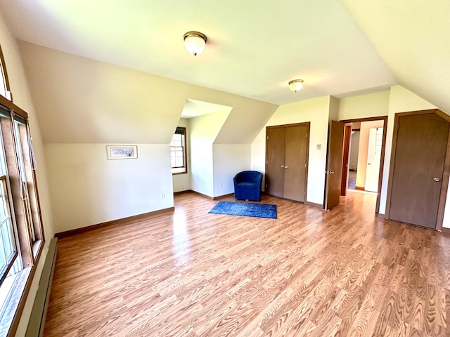 additional living space with light wood-style floors, a baseboard radiator, baseboards, and vaulted ceiling