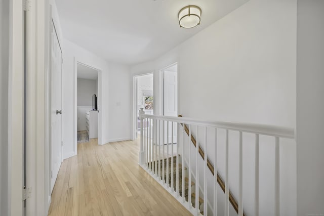 corridor featuring baseboards, light wood finished floors, and an upstairs landing
