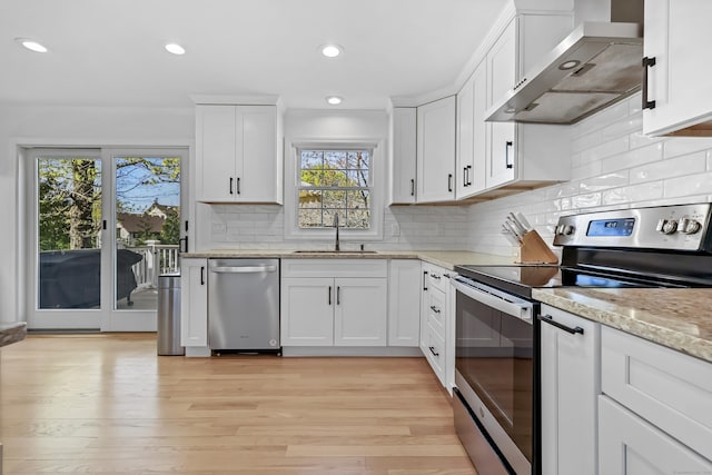 kitchen with a sink, wall chimney exhaust hood, appliances with stainless steel finishes, and a healthy amount of sunlight