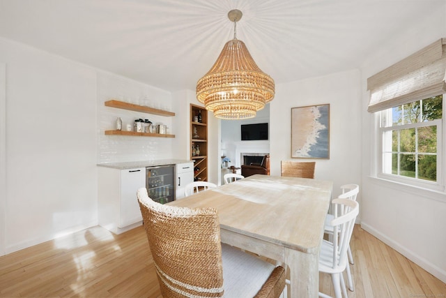dining area featuring an inviting chandelier, baseboards, beverage cooler, a bar, and light wood-style flooring