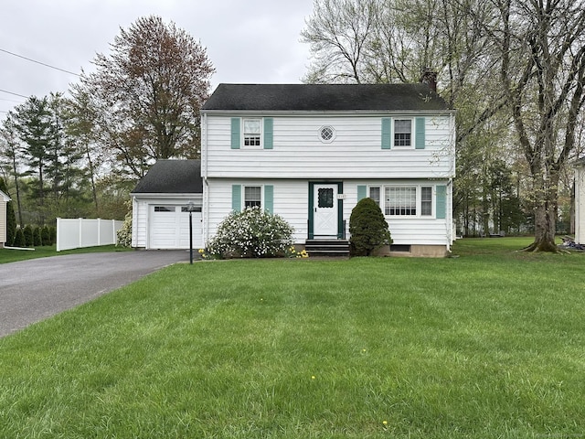 colonial house featuring fence, a front yard, entry steps, a chimney, and driveway