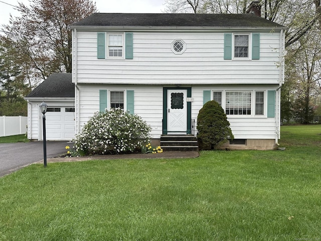 colonial inspired home featuring fence, a front yard, a chimney, entry steps, and driveway