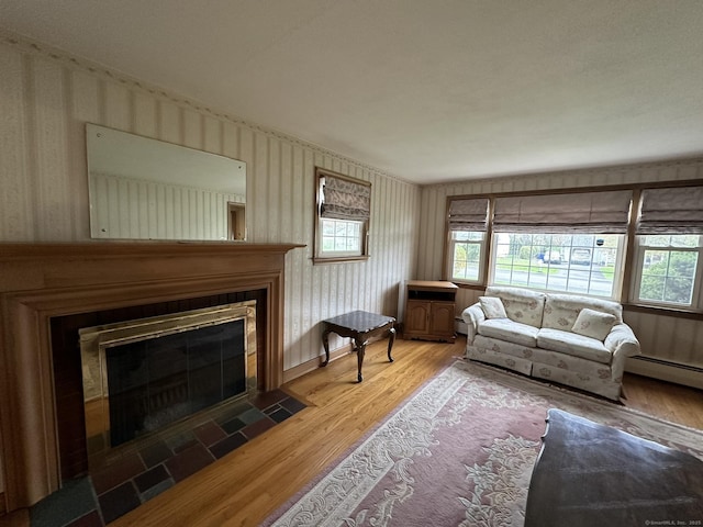 living room featuring a fireplace with flush hearth, a baseboard radiator, wood finished floors, and a wealth of natural light