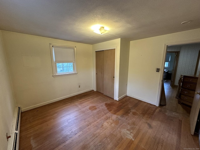 unfurnished bedroom featuring a textured ceiling, baseboards, a baseboard heating unit, and wood finished floors