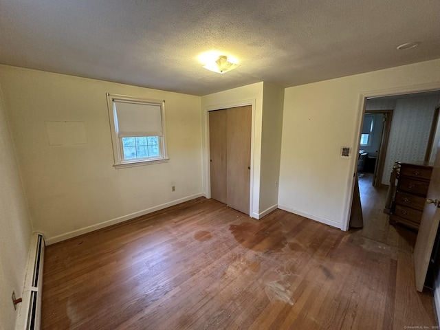 unfurnished bedroom with a closet, wood finished floors, baseboards, a textured ceiling, and a baseboard radiator
