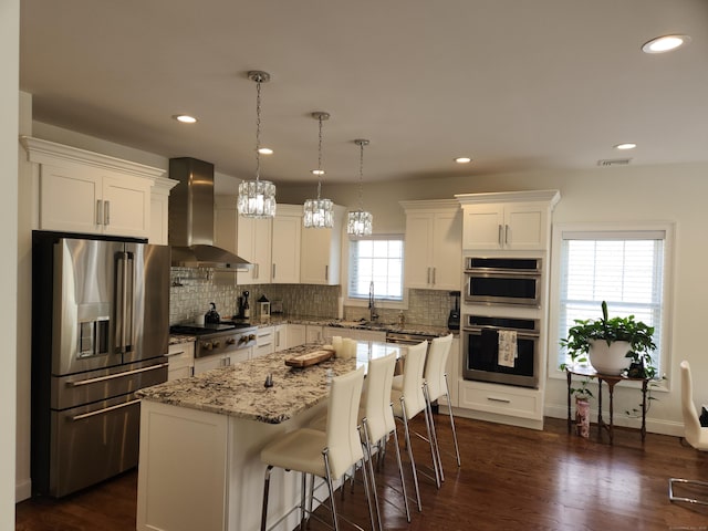 kitchen featuring wall chimney range hood, stainless steel appliances, decorative backsplash, and white cabinetry