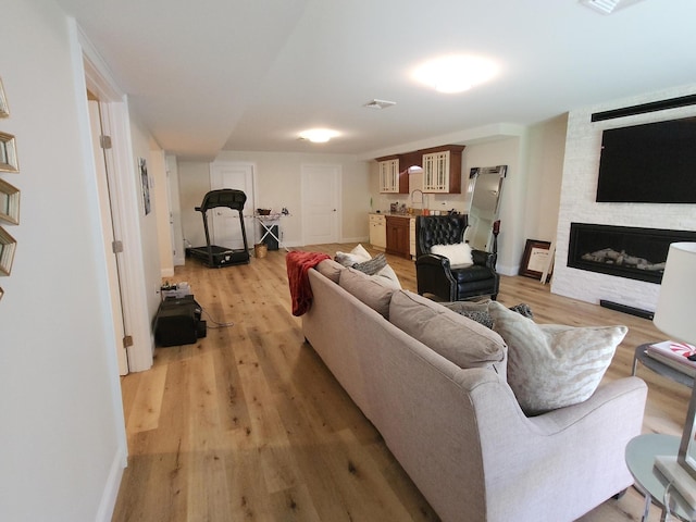 living room with a fireplace, baseboards, visible vents, and light wood-style floors