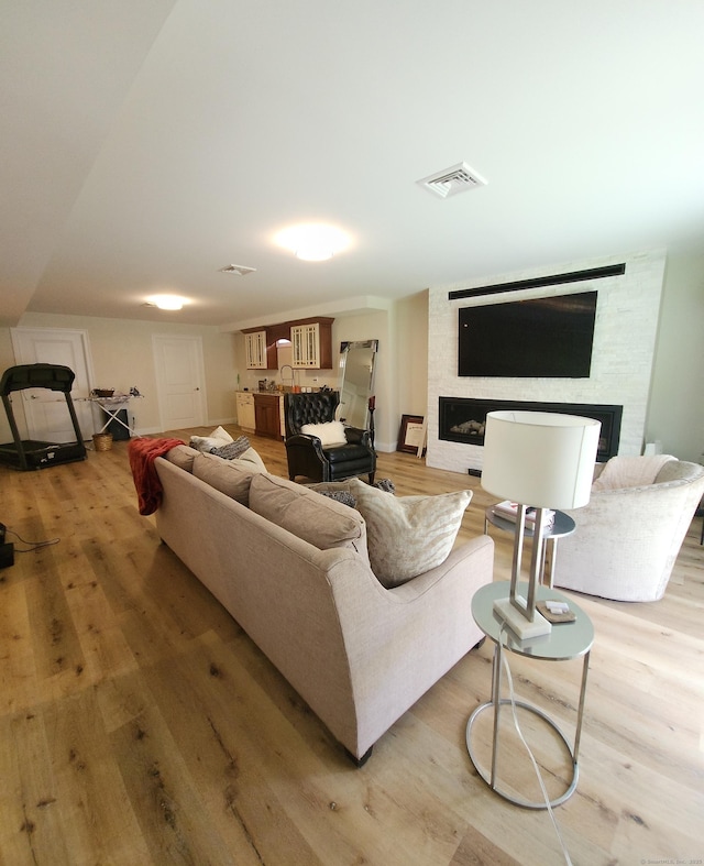 living room featuring a fireplace, light wood-style flooring, and visible vents